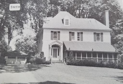 Black and white photo of Sister Mildred Hawkins Hall in Spring or Summer. The porch is closed in and features a long awning. A garage sits to the right.